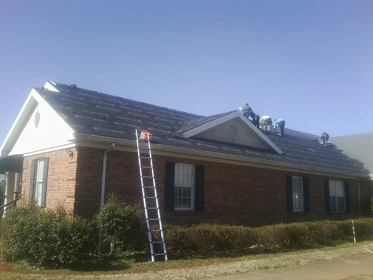 Crew tearing shingles off a brick ranch roof with a ladder set — Metal Roof Repair work by our crew in Limestone