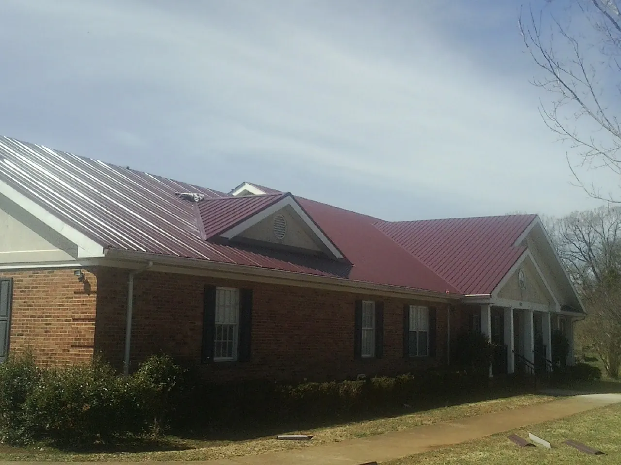 Red metal roof with gabled entries on a long brick building, from a Hail Damage Roof Repair job in Limestone