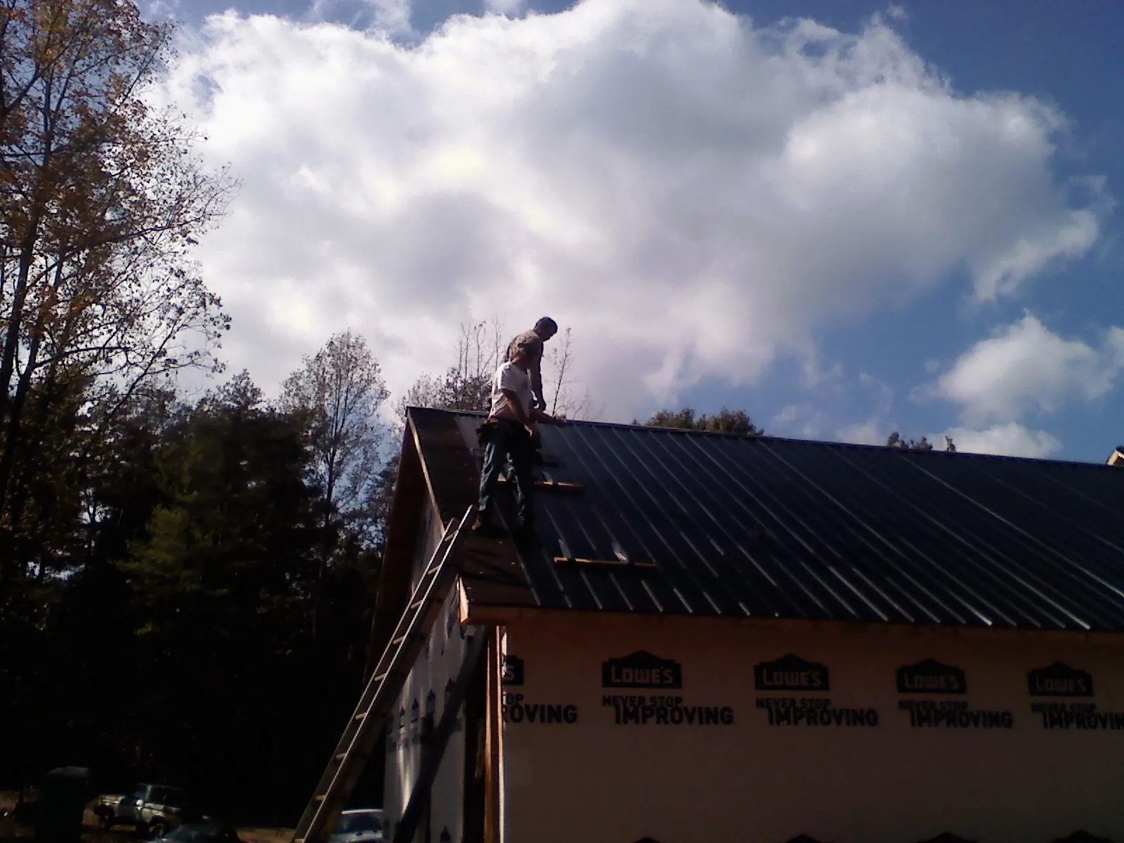 Roofer fastening dark metal panels high against a cloudy sky, from a Roof Inspection job in Limestone