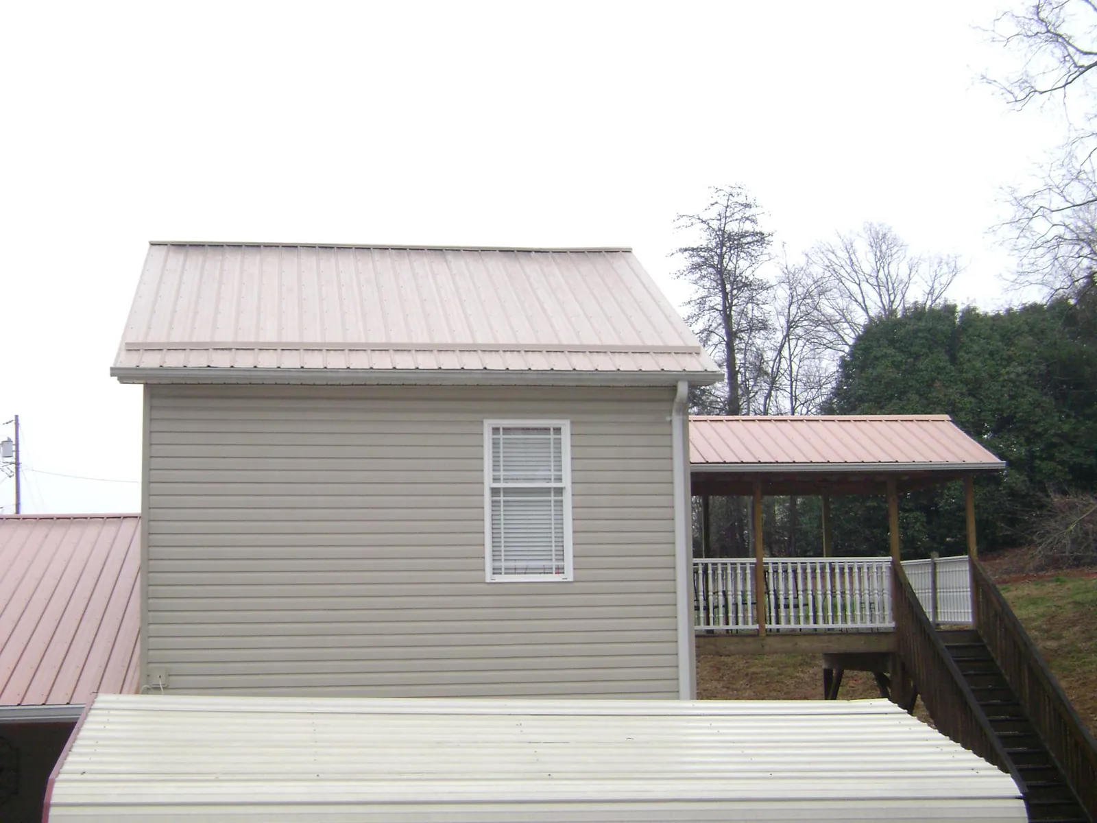 Tan metal roofs on a two story addition and attached porch, from a Roof Replacement job in Limestone